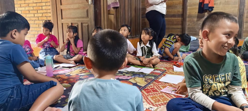 Children of the English class sitting together on the floor of the hut, working with exercise books